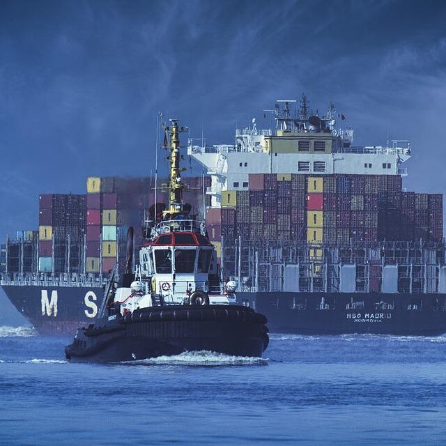 Photo of a cargo ship and a tug boat in the ocean 