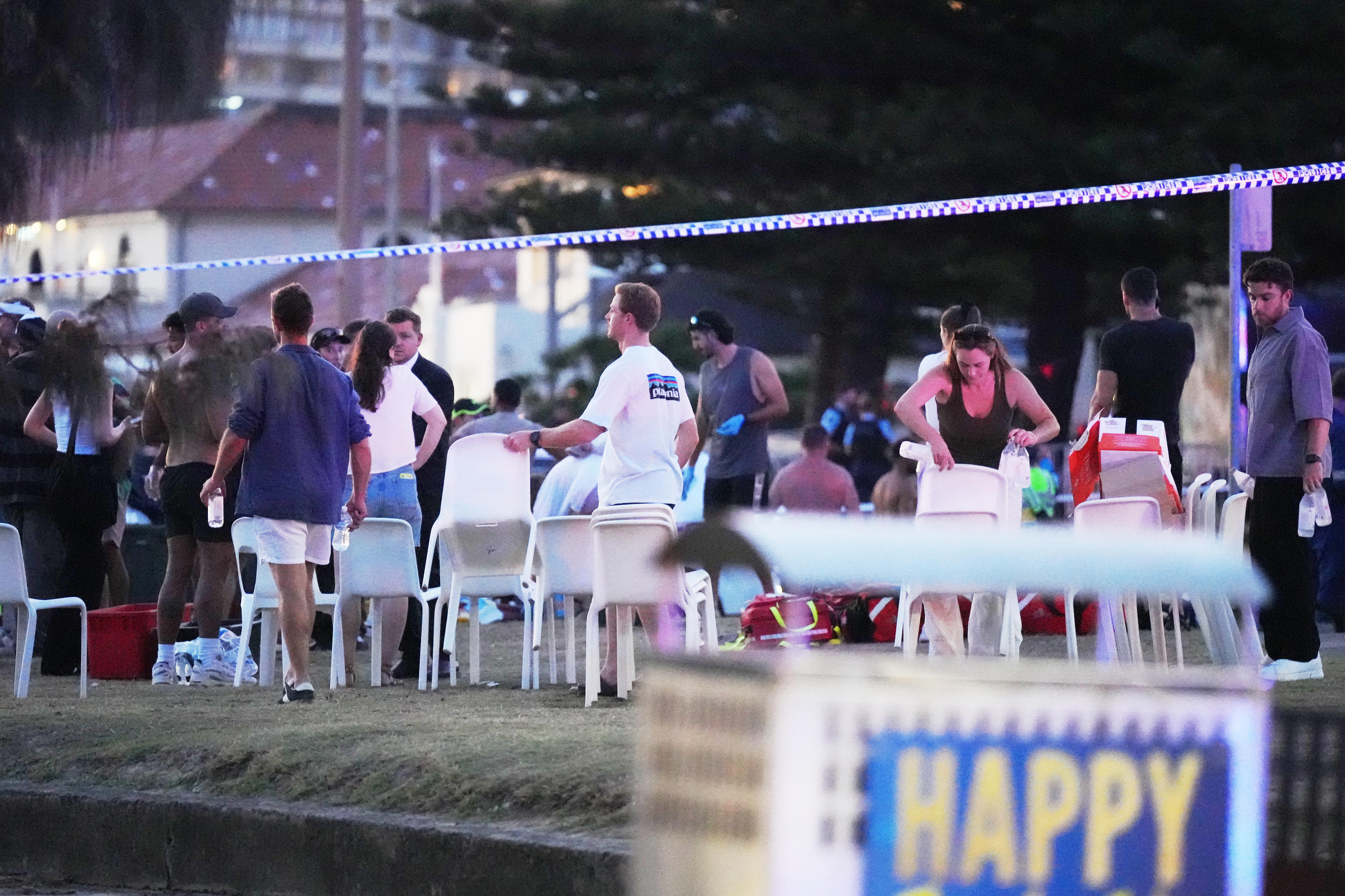 Pessoas no local do tiroteio em Bondi Beach com a polícia isolando a área