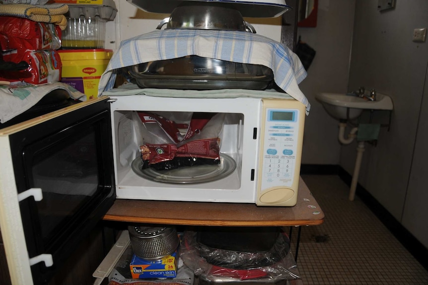 The remains of a barbecue chicken in its original bag sit inside an open microwave, on a cluttered counter