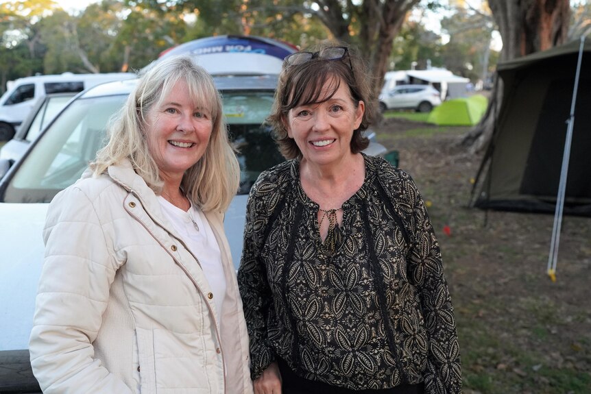 Two women stand at a campground. A brown tent is seen in the background