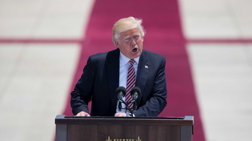Donald Trump speaks at a lectern in with a Menora emblazoned on it