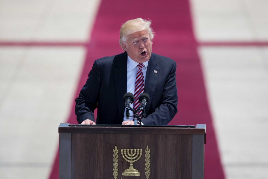 Donald Trump speaks at a lectern in with a Menora emblazoned on it