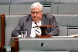 Clive Palmer looks downwards as he sits the House of Representatives Chamber.