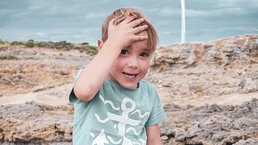 A young boy smiling at the camera with his hand on his head