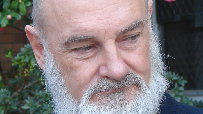 An older, blading man with a greyish white beard glancing to his left.
