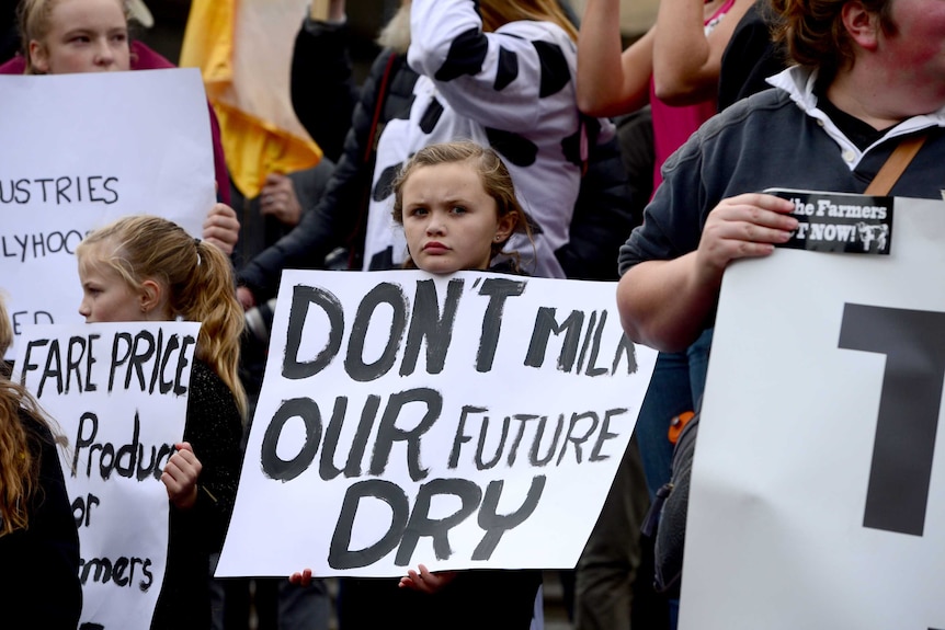 Two children holding placards saying 'don't milk our future dry', 'fare price' stand among a crowd of protesters.