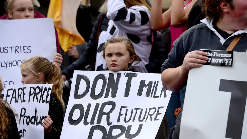 Two children holding placards saying 'don't milk our future dry', 'fare price' stand among a crowd of protesters.