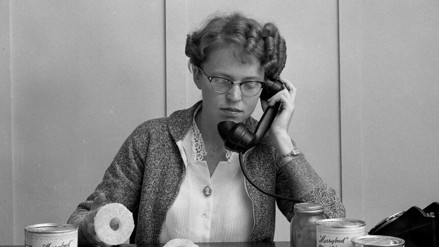 Black and white photo of a woman on the phone at her desk.