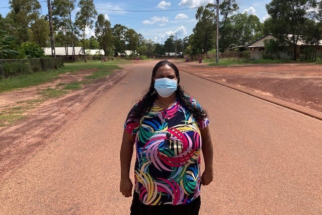 A woman wearing a facemask stands in the middle of a long street.
