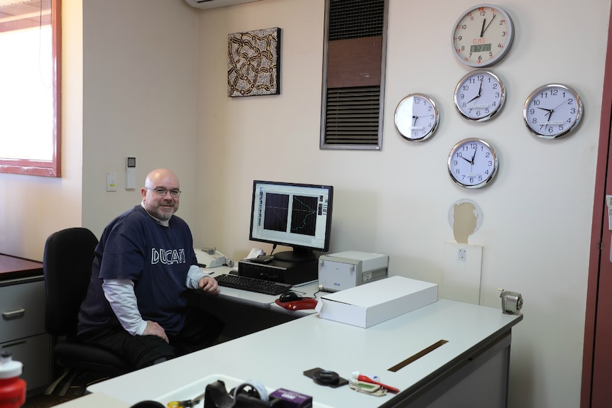 Weather observer and manager of the Giles Weather Station sits at his desk beside multiple clocks.