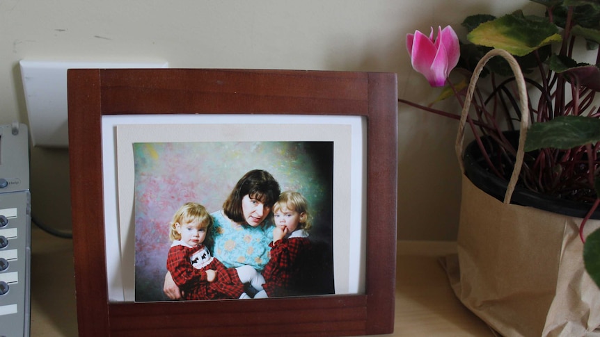 A photo of a mother with two young children in a picture frame with the glass cover removed.