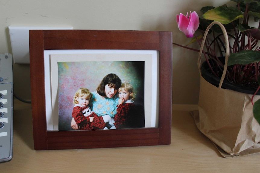 A photo of a mother with two young children in a picture frame with the glass cover removed.
