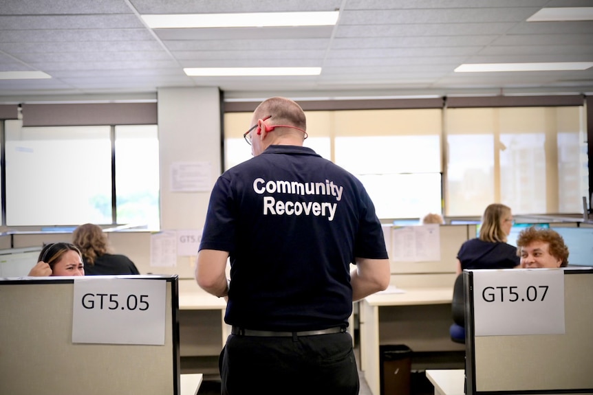 A man with 'community recovery' on his shirt stands in an office