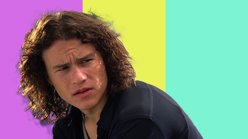 Heath Ledger in the 1990s movie 10 Things I Hate About You in front of a purple, yellow and aqua background wearing 90s fashion.