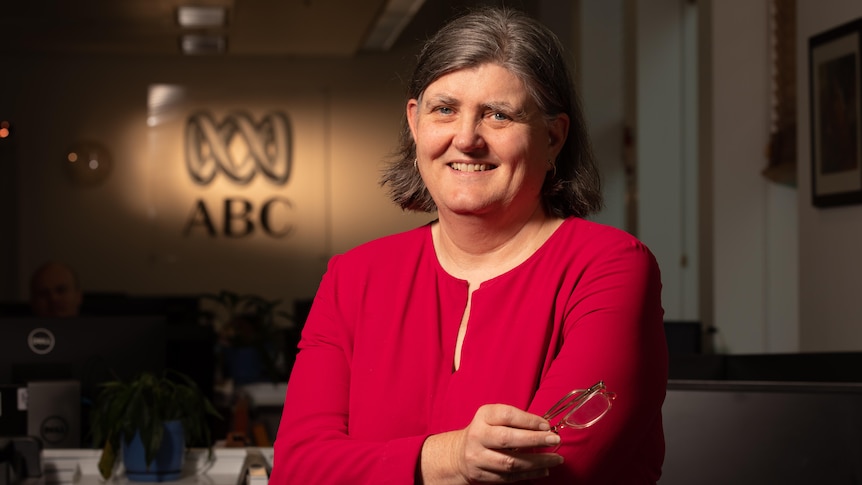 Woman in red top smiling at camera, holding glasses, wtih ABC logo in background.