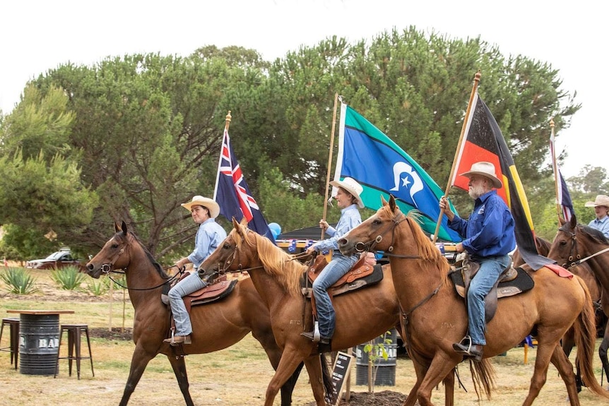 Three riders holding flags for Australia Day on top of ex-racehorses