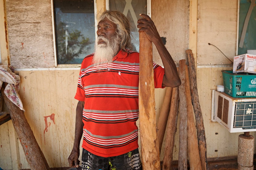 A man holds a didgeridoo in front of a house.