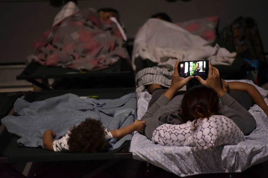 A woman and a child rest on cots while waiting at Humacao Arena refugee centre.