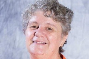 A woman with short curly grey hair wearing an orang blouse smiling