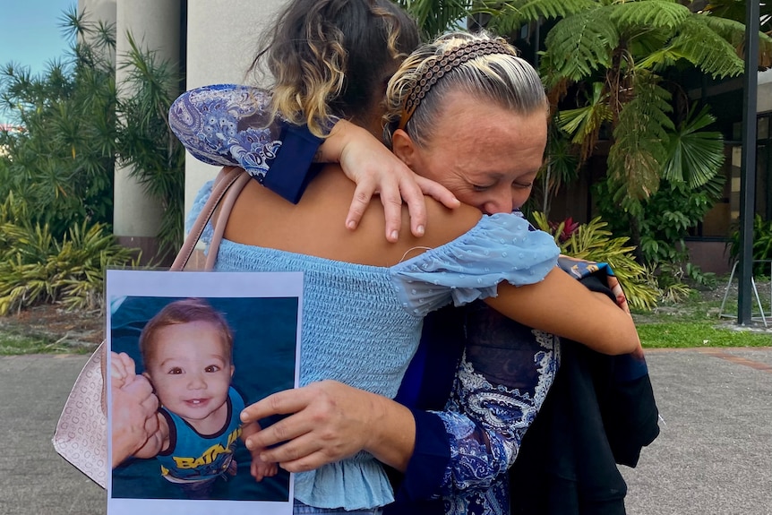 Two woman hugging. one is crying and holding a photo of a baby