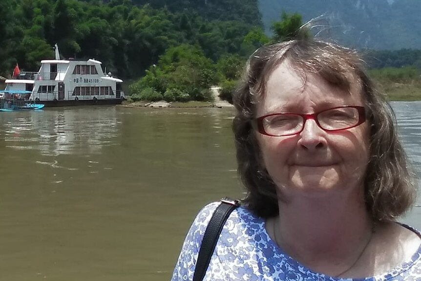A woman with red glasses standing in front of a boat and islands.