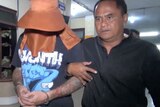 A man of Indonesian appearance leads a handcuffed tattooed man with a hooded hat hiding his face.