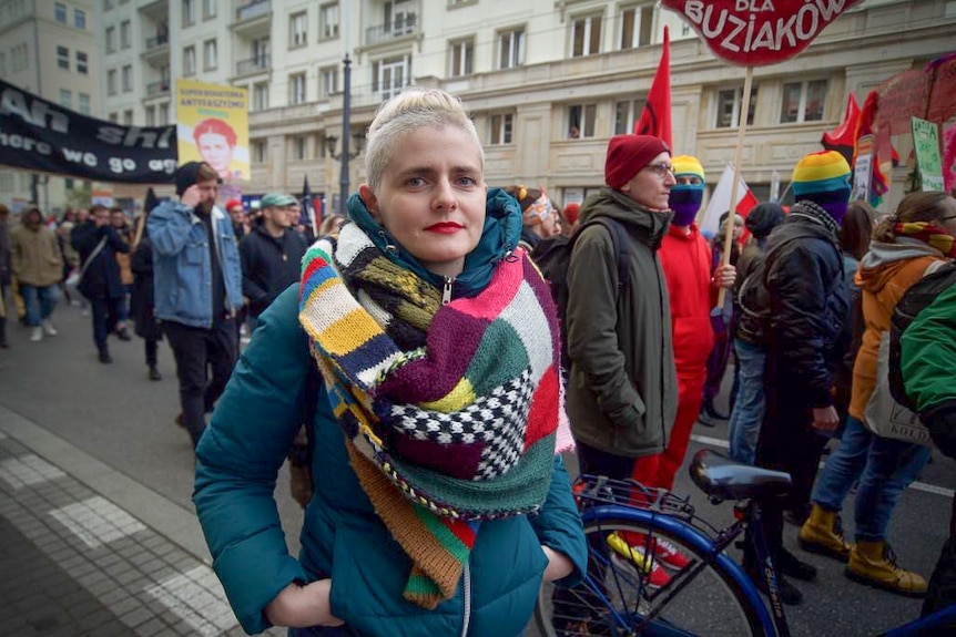 A woman in a colourful scarf stands in a protest in Warsaw