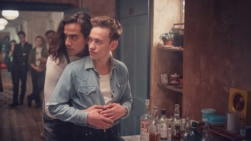 A still from the miniseries It's a Sin with two young men hugging at a grimey house party in the 80s