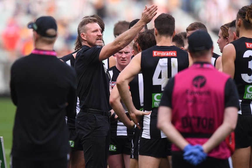 Un entraîneur de l'AFL montre du doigt alors qu'il donne une conférence d'équipe au milieu de l'ovale pendant un match.