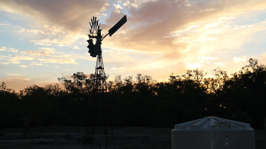 The silhouette of a windmill against an orange sunset