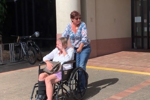 Amanda Jane White is  being pushed in a wheelchair by a friend, and covers her face outside the Supreme Court in Cairns.