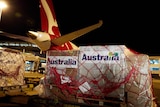 A Qantas plane sits on a tarmac, being loaded with wrapped containers of COVID-19 supplies