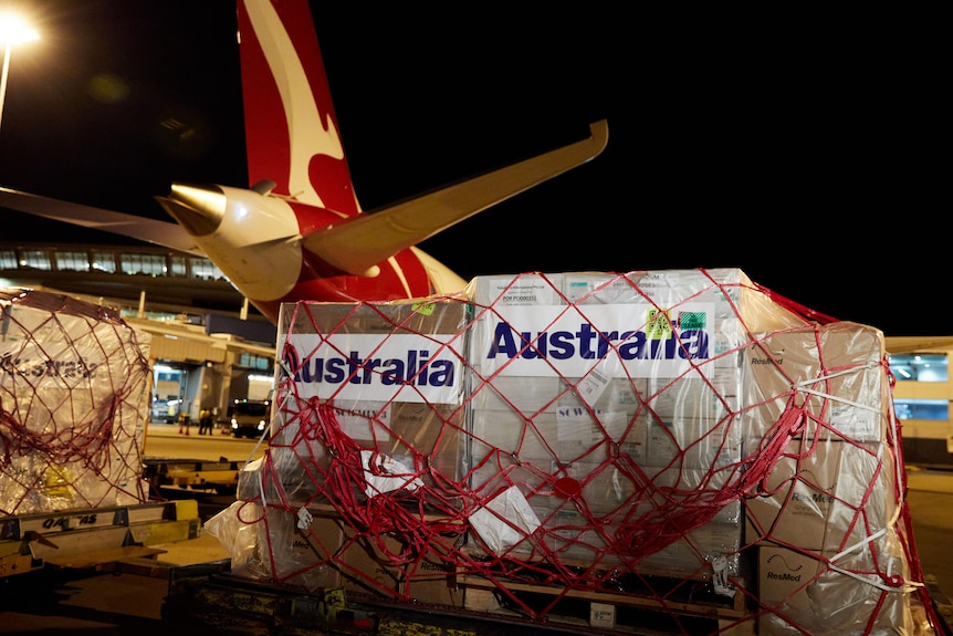 A Qantas plane sits on a tarmac, being loaded with wrapped containers of COVID-19 supplies