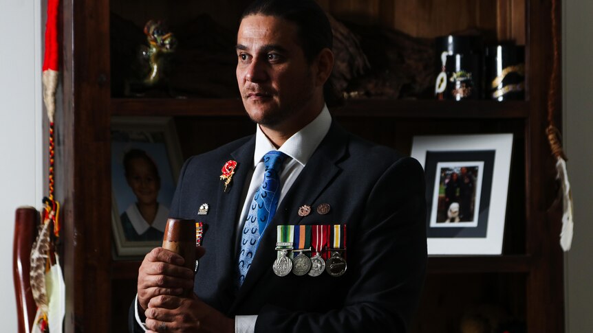 A man in a suit with military medals holding a didgeridoo.