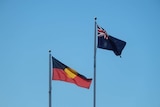 An Australian and Aboriginal flag flying in the wind on a flagpole.