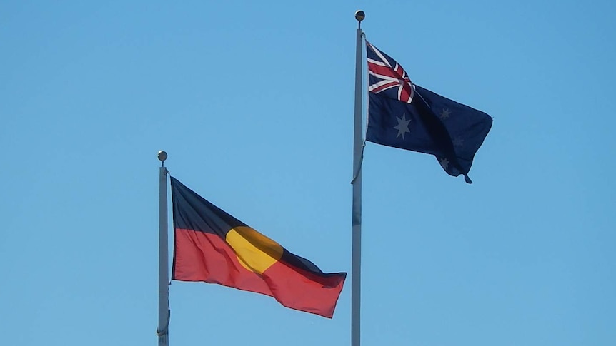 An Australian and Aboriginal flag flying in the wind on a flagpole.