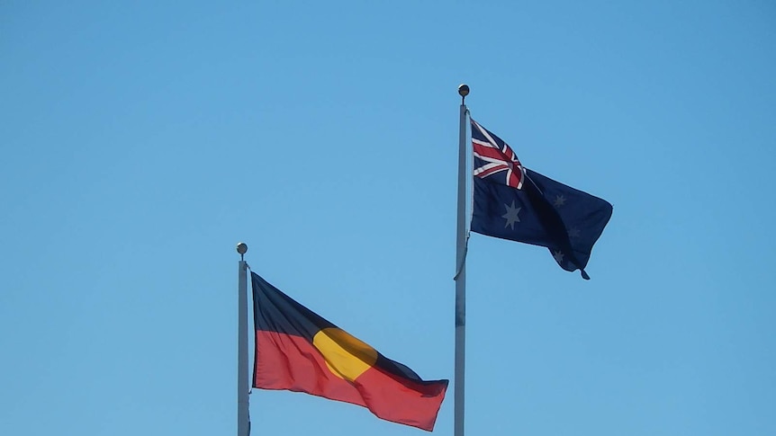 An Australian and Aboriginal flag flying in the wind on a flagpole.