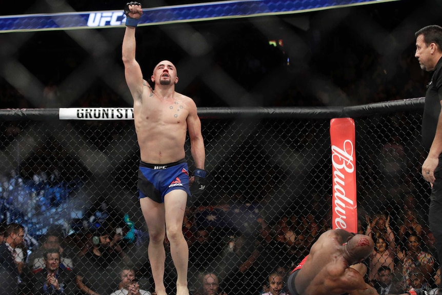 Robert Whittaker walking with his right arm held in the air inside the Octagon after beating Yoel Romero.