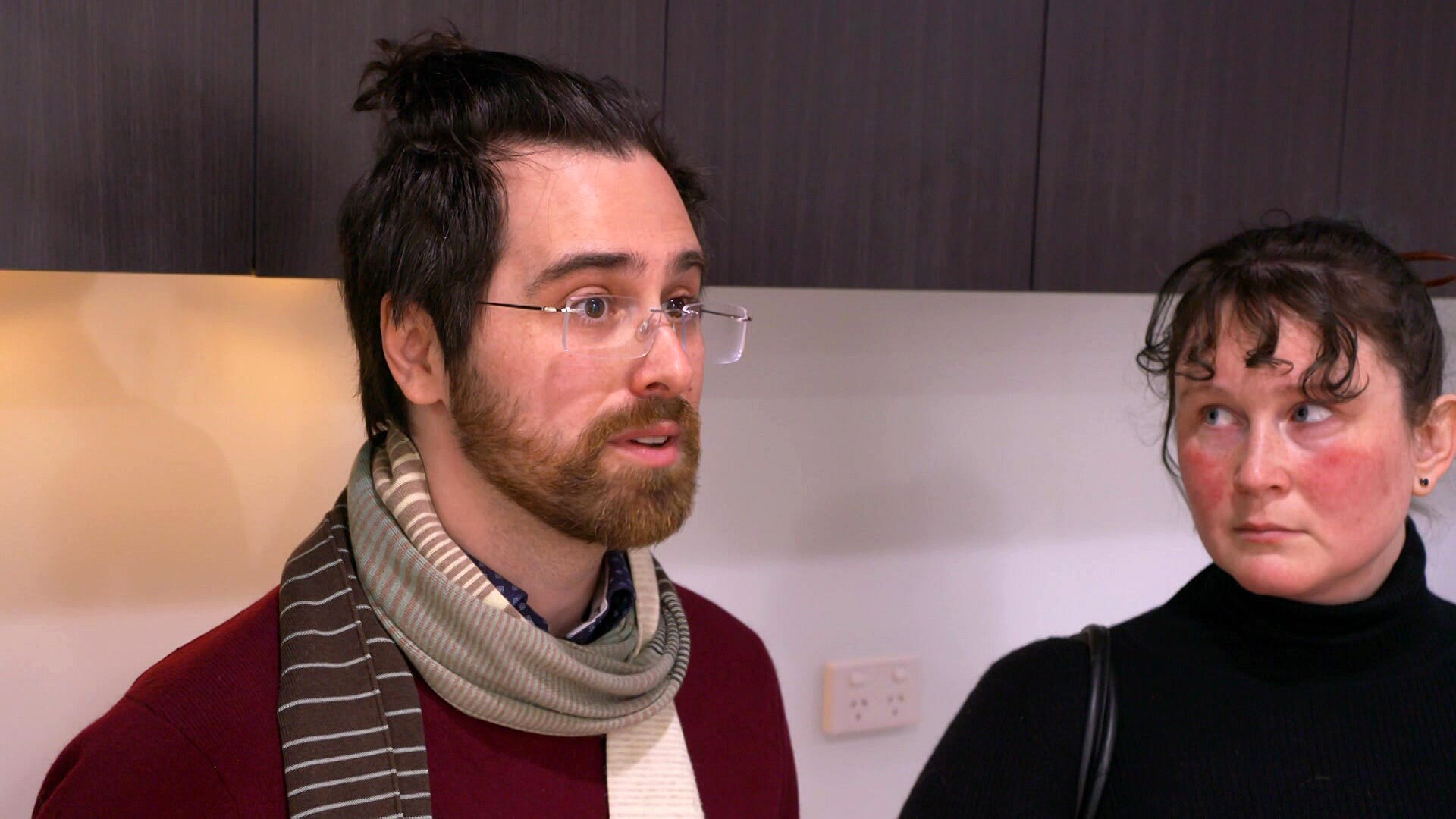 A man wearing a striped scarf standing next to a woman wearing a black top.