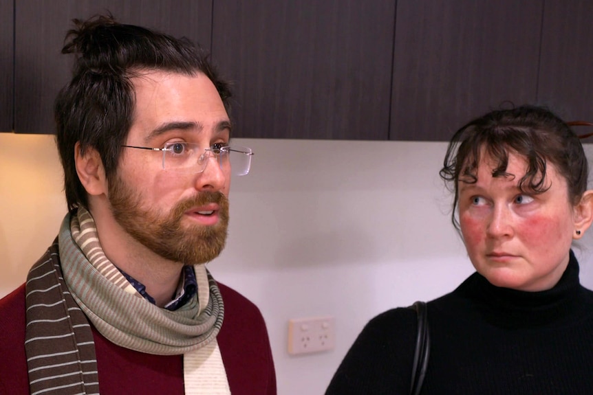 A man wearing a striped scarf standing next to a woman wearing a black top.