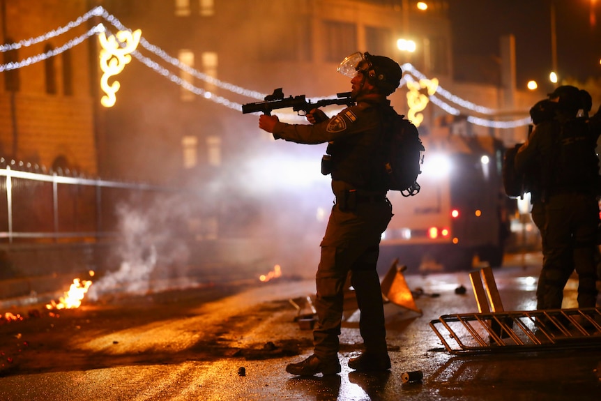 An Israeli police officer aims his rifle towards Palestinian demonstrators