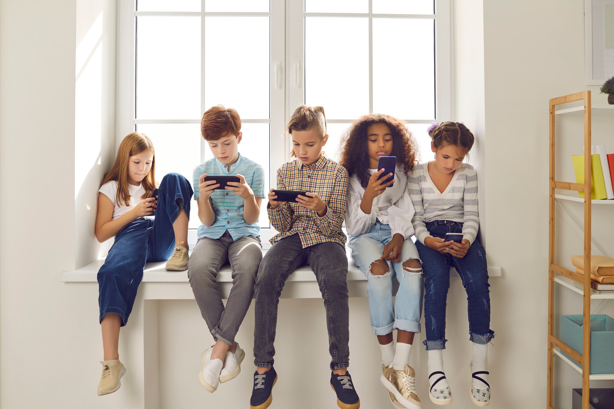 Children are lined up on bench using phones rather than talking