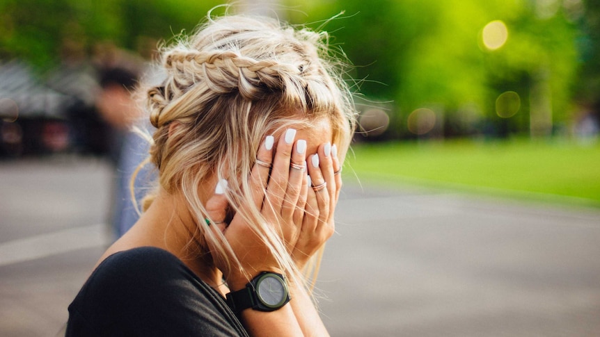 A woman covers her face with her hands, for a story about work rights and the JobKeeper scheme.