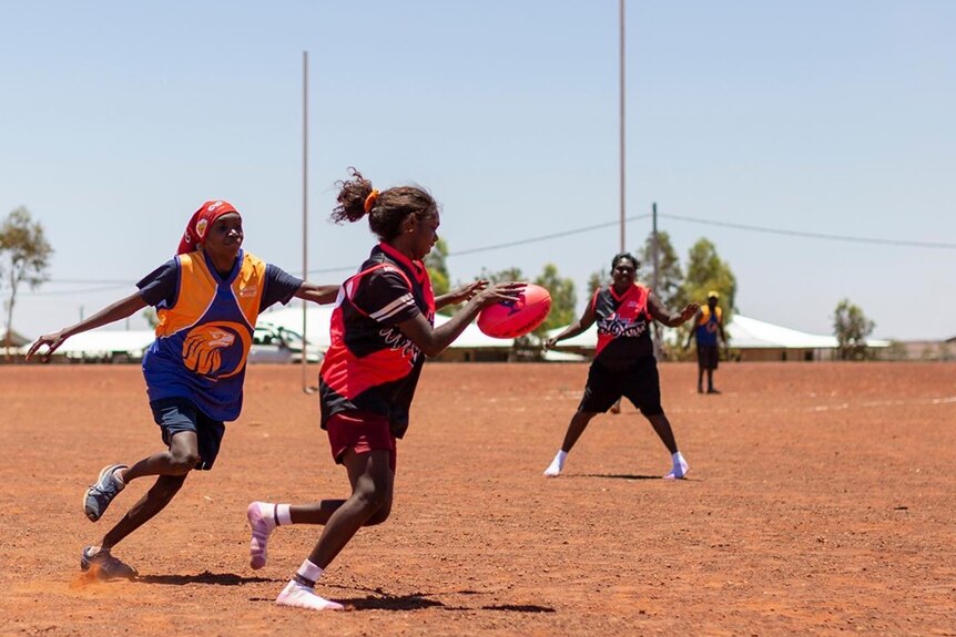 Women playing Australia Rules Football on a dirt field in Balgo.