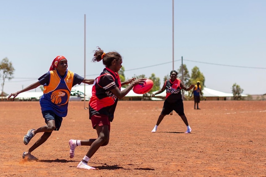 Women play football on a dirt field in Balgo.