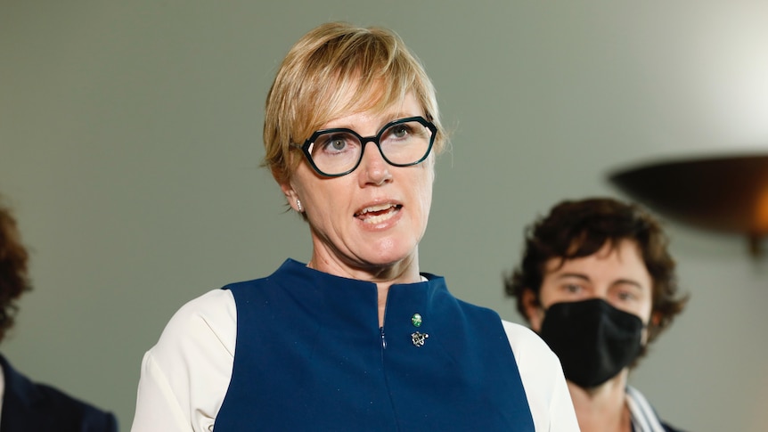 A woman in a blue top and glasses speaks