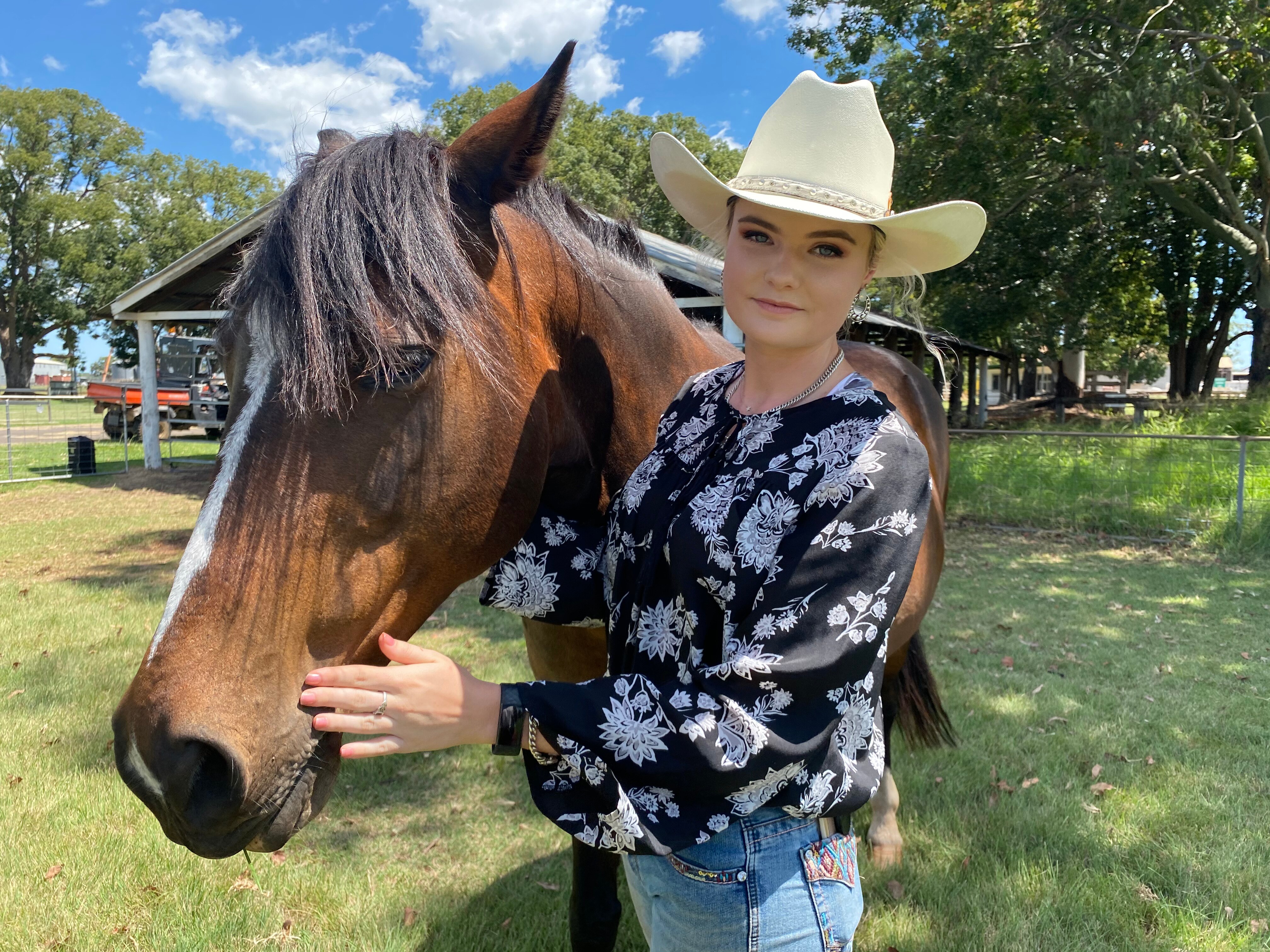 A young woman in a cowboy hat stands next to a horse.