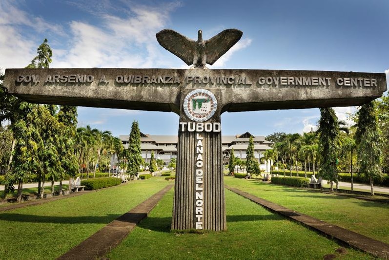 A t-shaped concrete statue with an eagle stretching at its apex marks the Lanao del Norte Capitol sitting on verdant lawns.