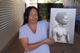 A woman  holding up a black and white photo of Dirrikaya