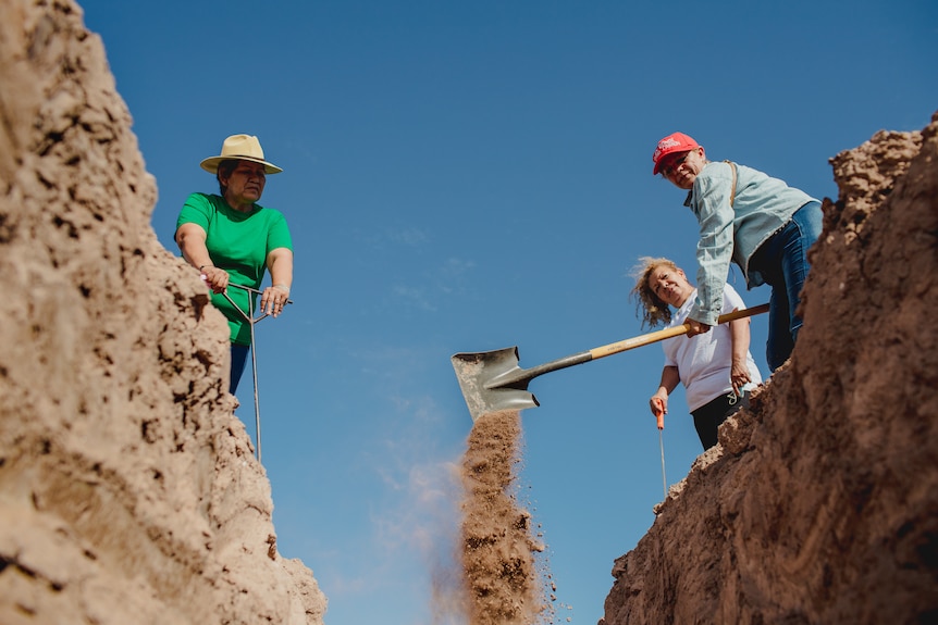 Three women shovel dirt.